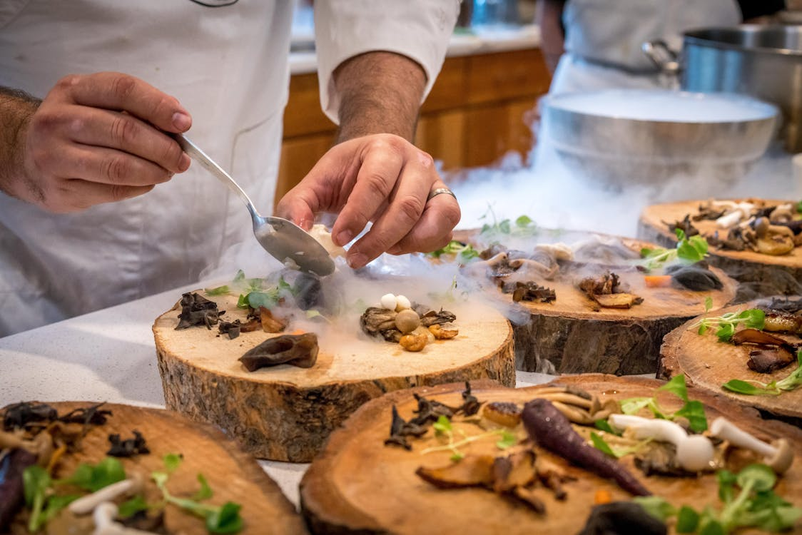 chef's hands placing food artisically onto carved wooden log platters