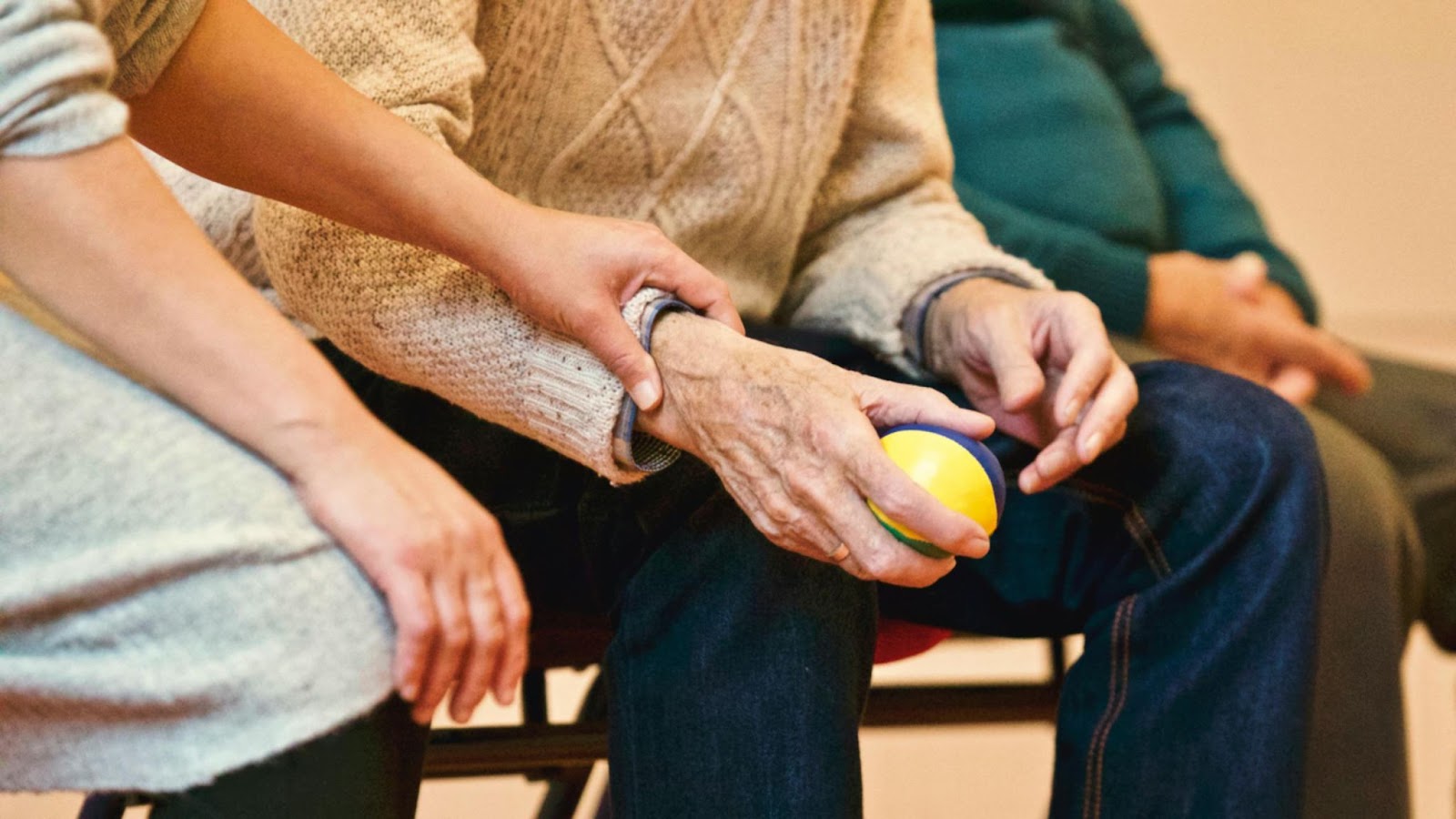 person holding onto the hand of old person sitting down with ball in hand
