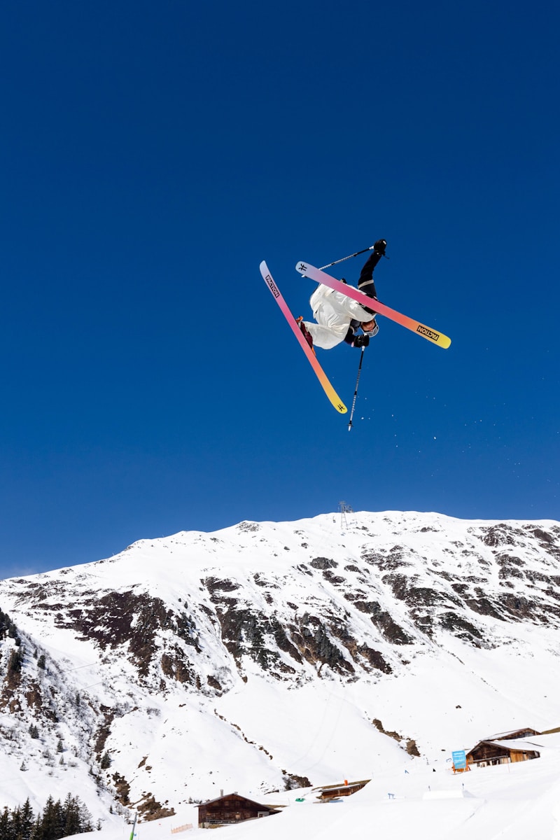 a man flying through the air while riding skis and bright blue sky and snow on mountain