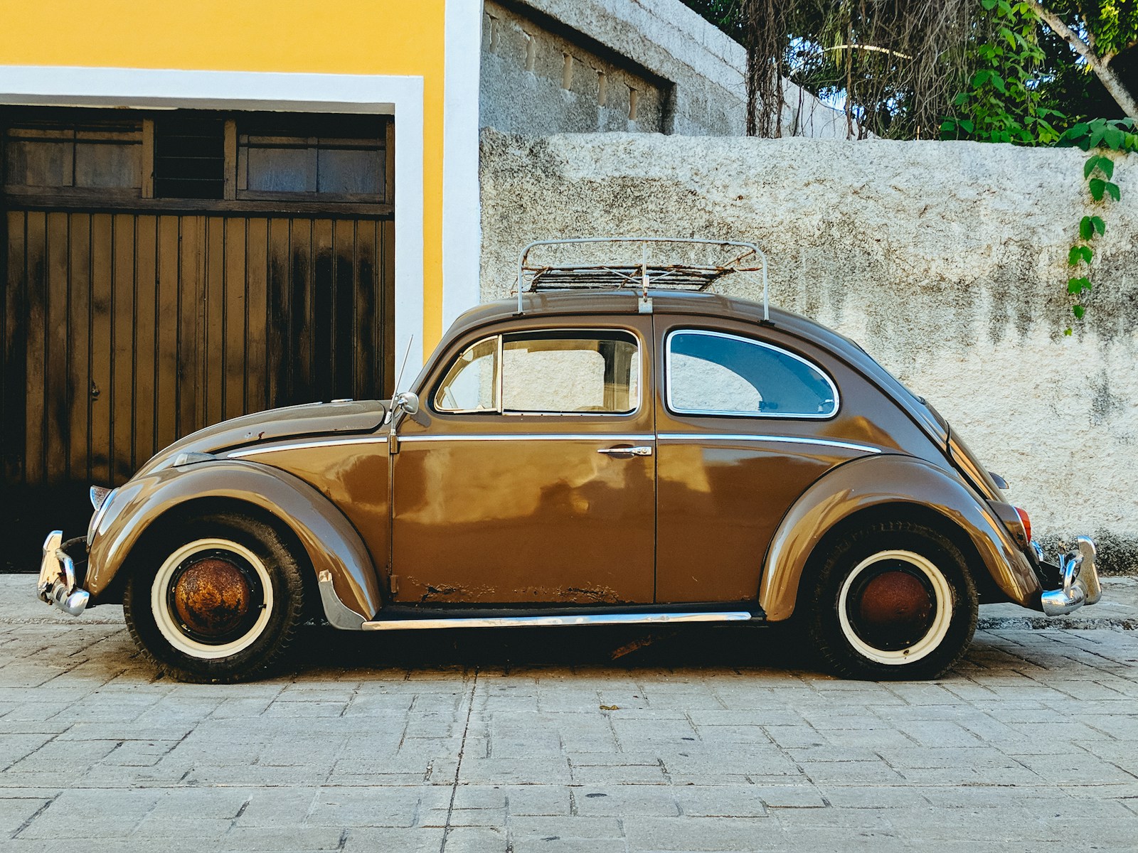 parked brown Volkswagen beetle in front of yellow wall and grey wall