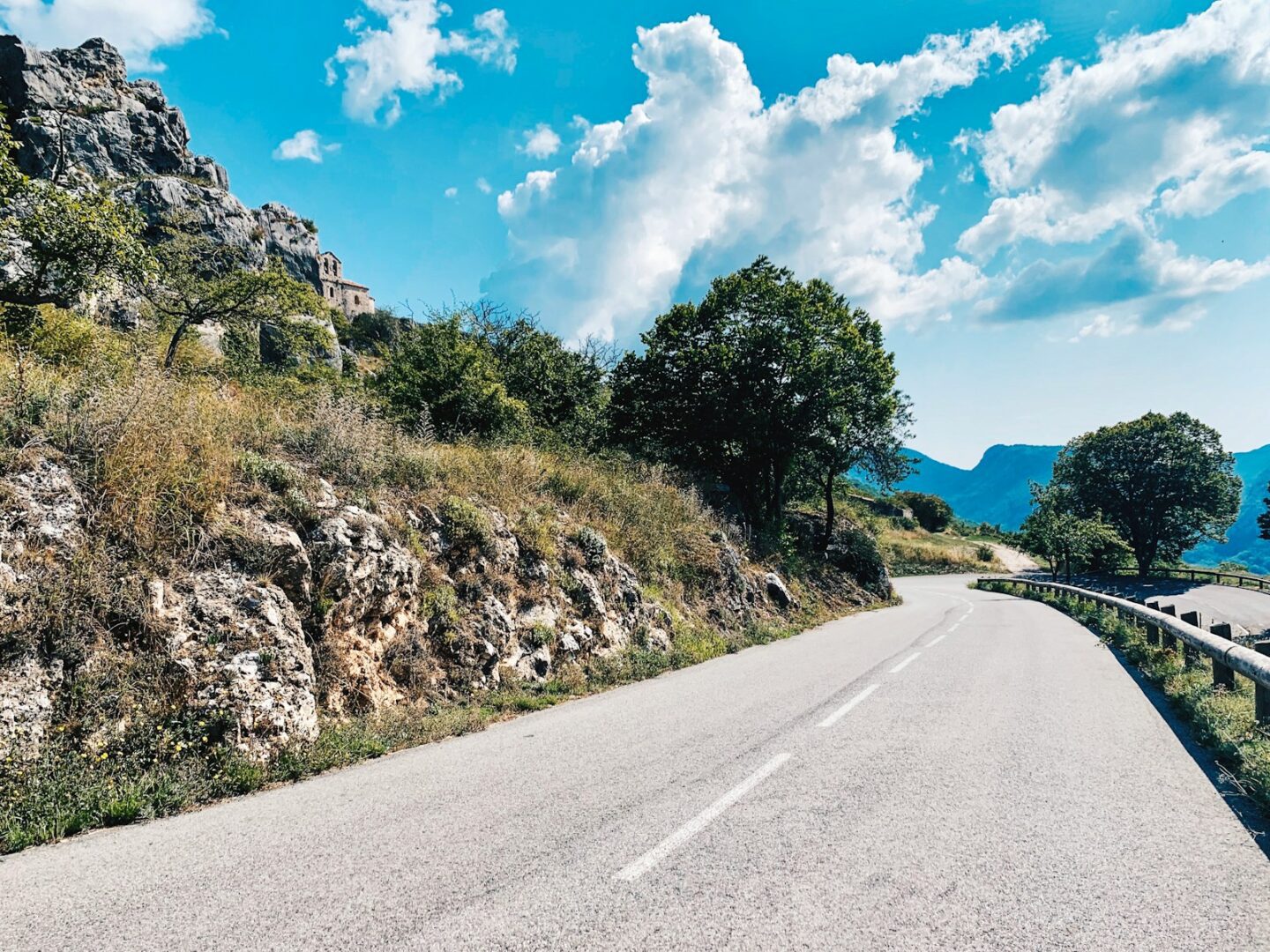 winding road on the side of a mountain slope with blue sky and clouds 