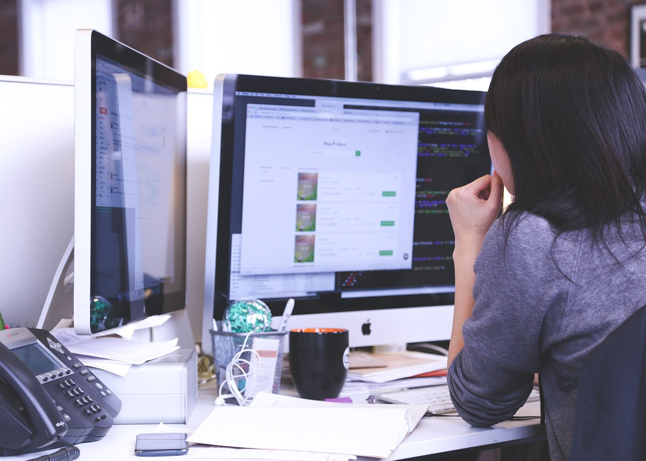 woman sitting at computer screen on desk with papers around her