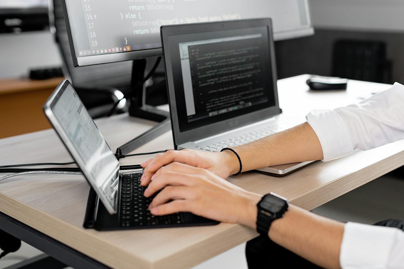 peson typing pn laptop with another laptop on desk next to it