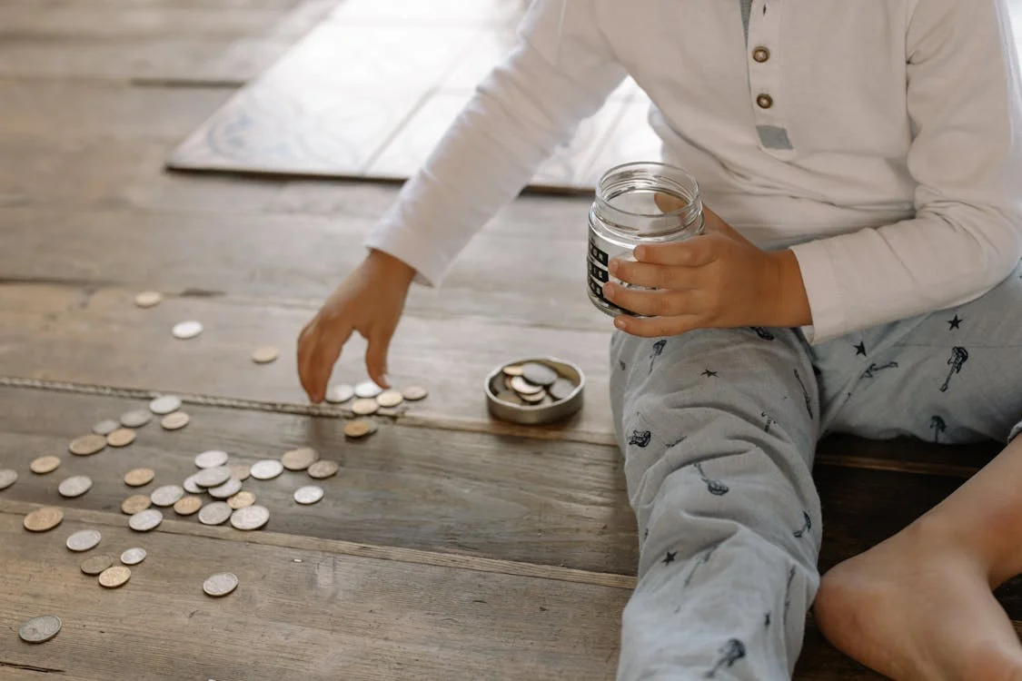 child sitting on the floor counting coins off the floor into a jar held in hand