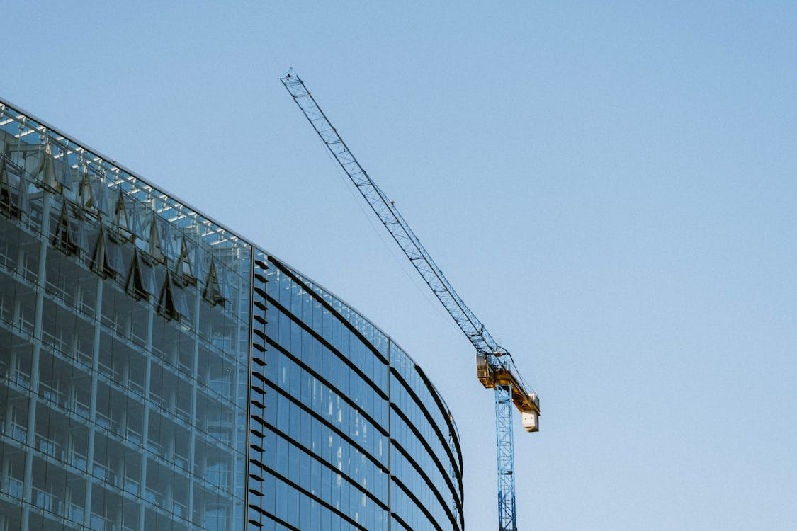 large glass building partially built with crane above it and lue sky