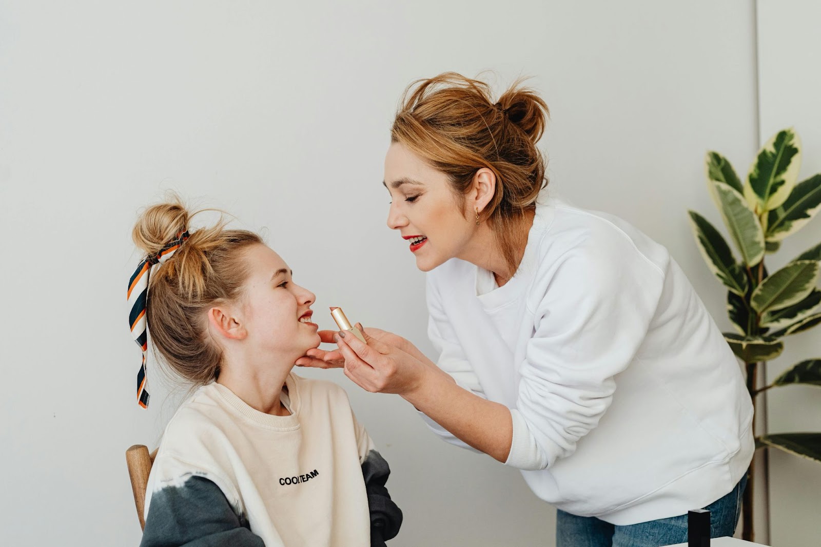 woman putting lipstick on young woman who is sat in chair