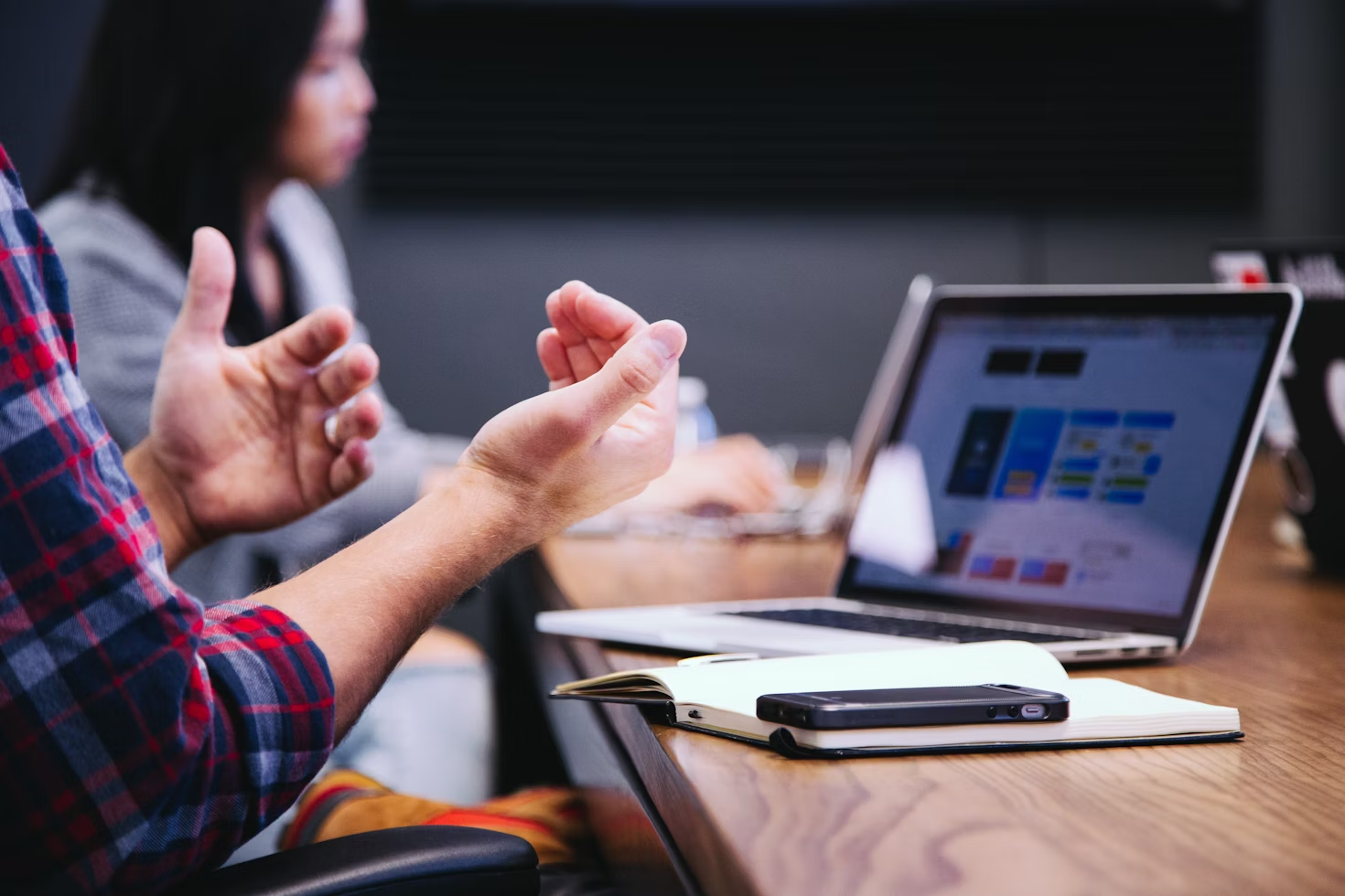 person gesturing with hands at desk with laptops