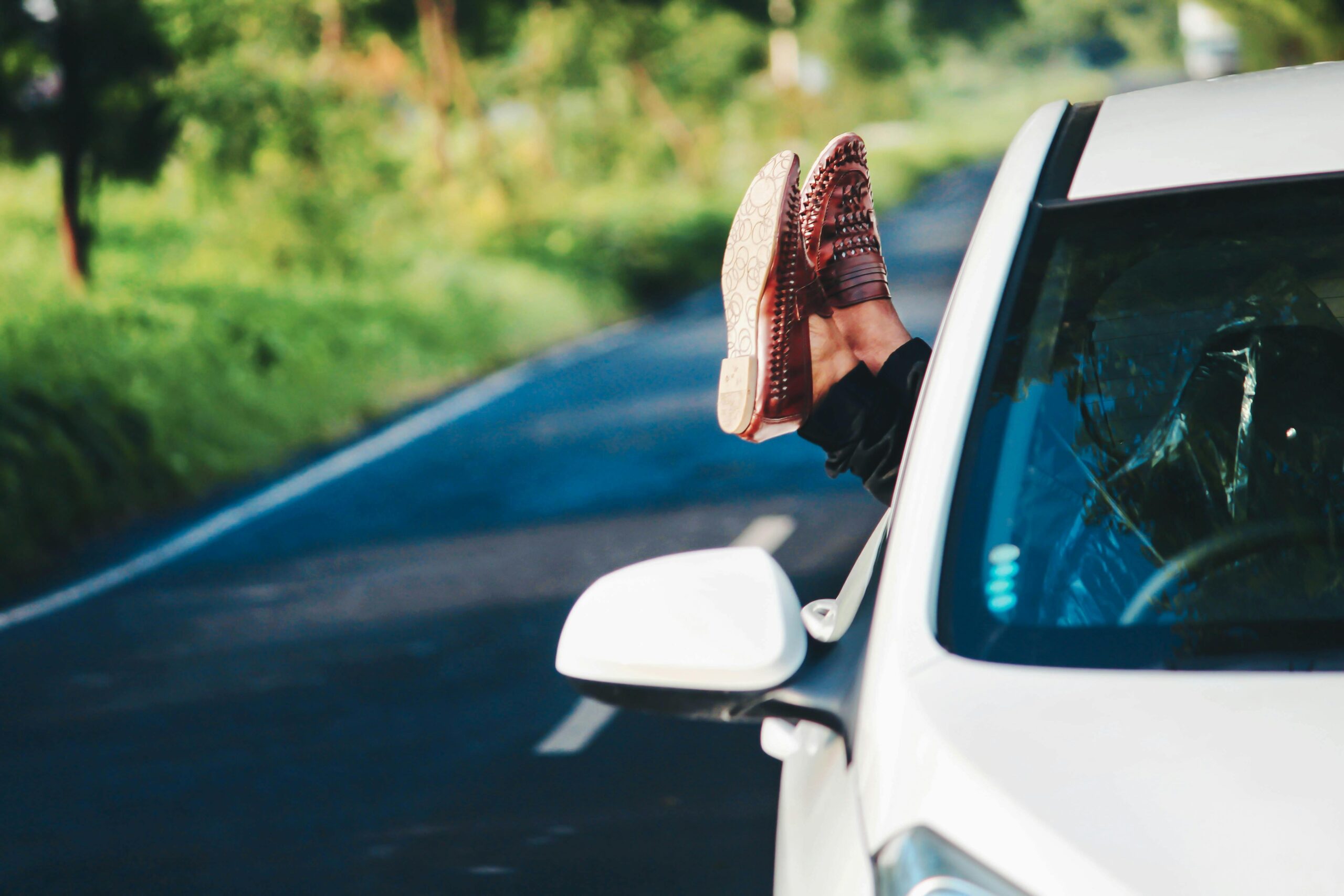 car on road with crossed legs sticking out of the window