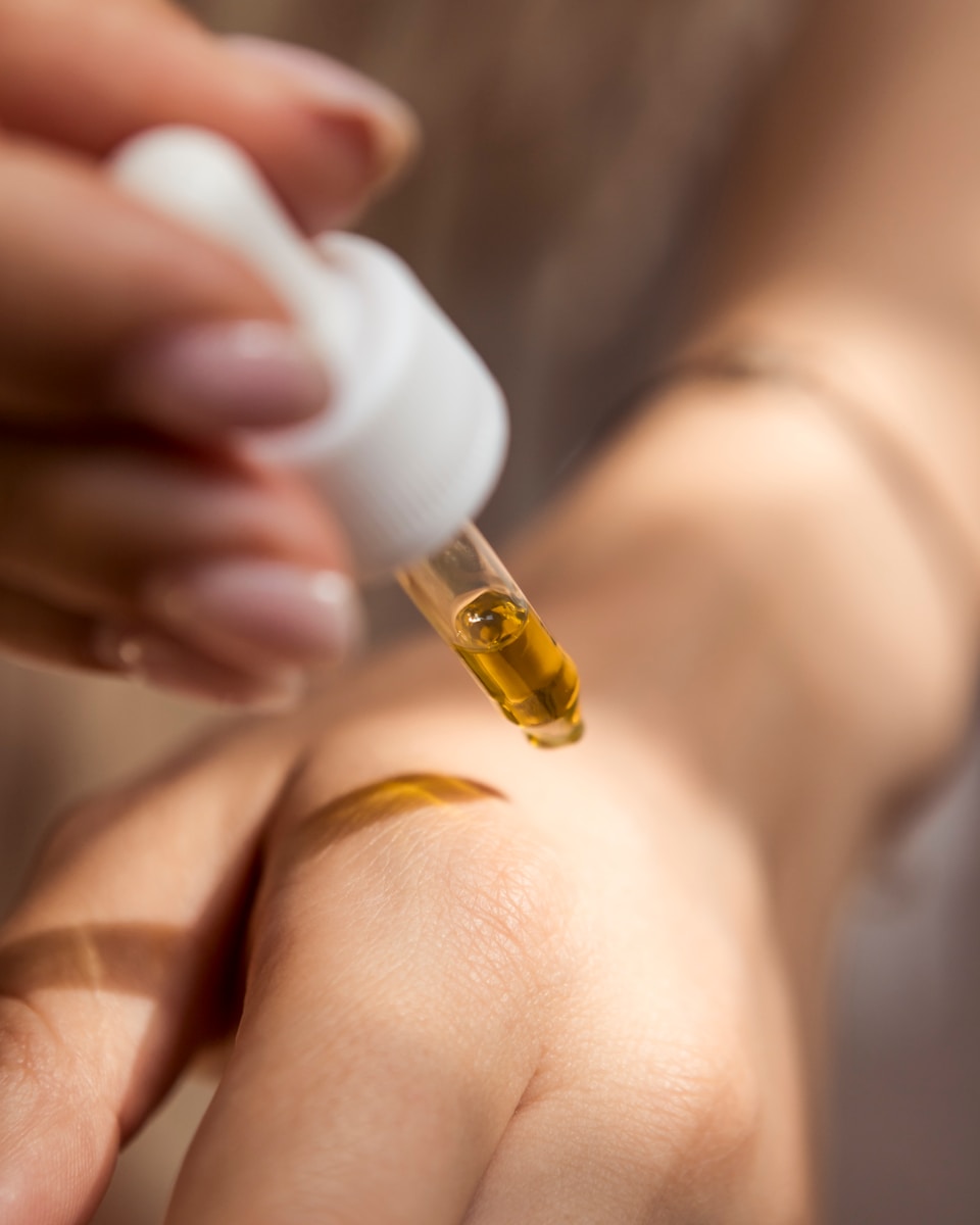person holding dropper with oil in it against hand