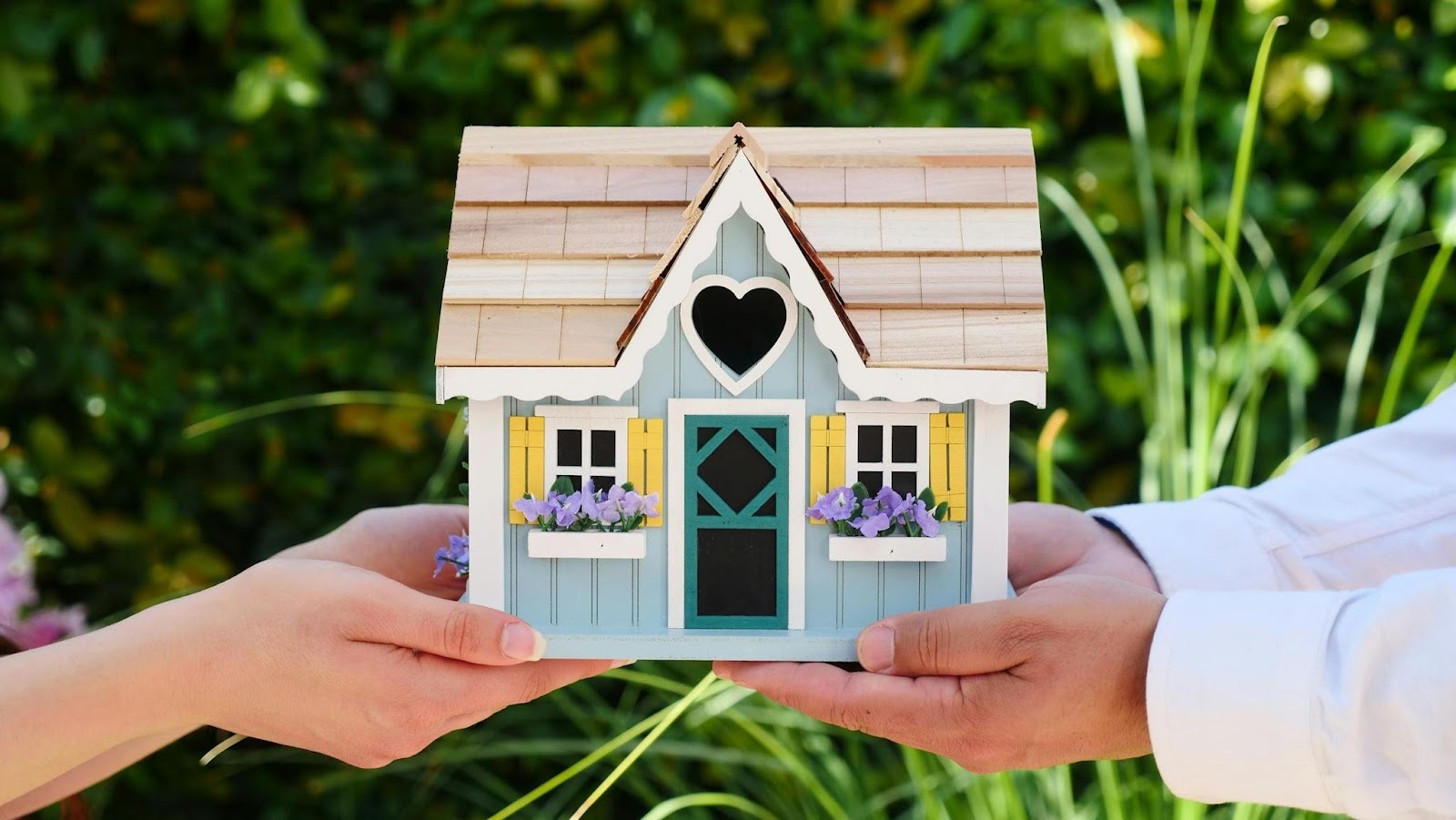 two hands holding colourful model house