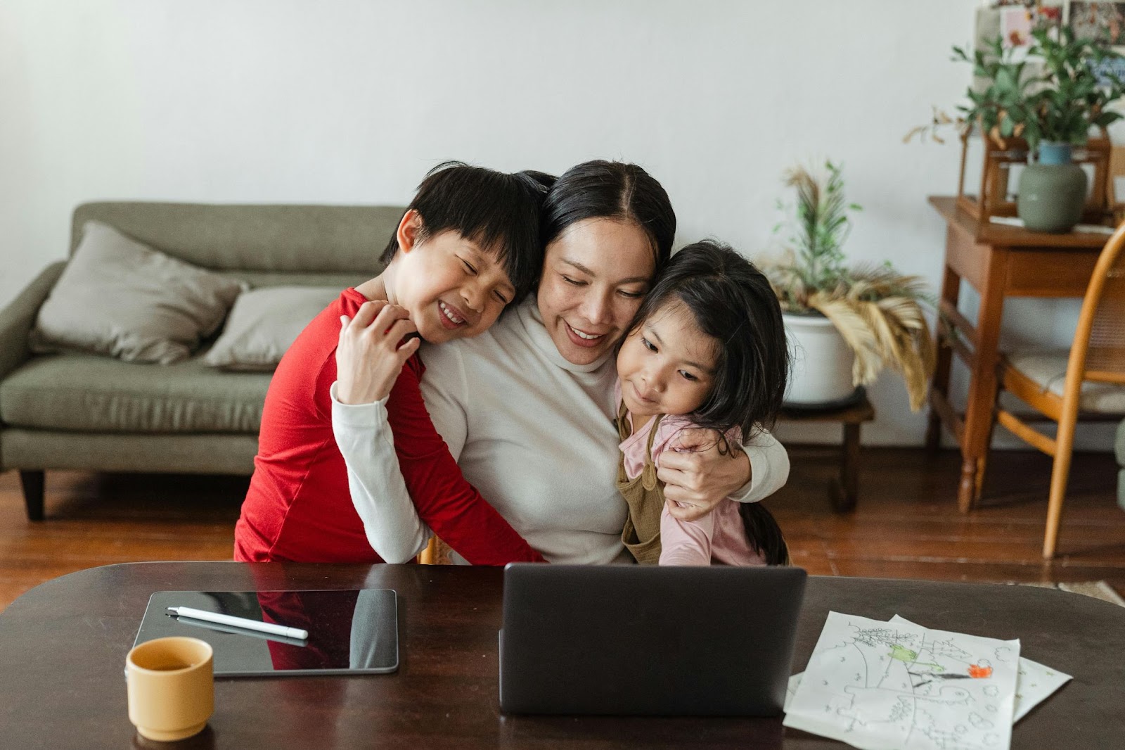 mum hugging a boy and a girl in living room and looking at a laptop