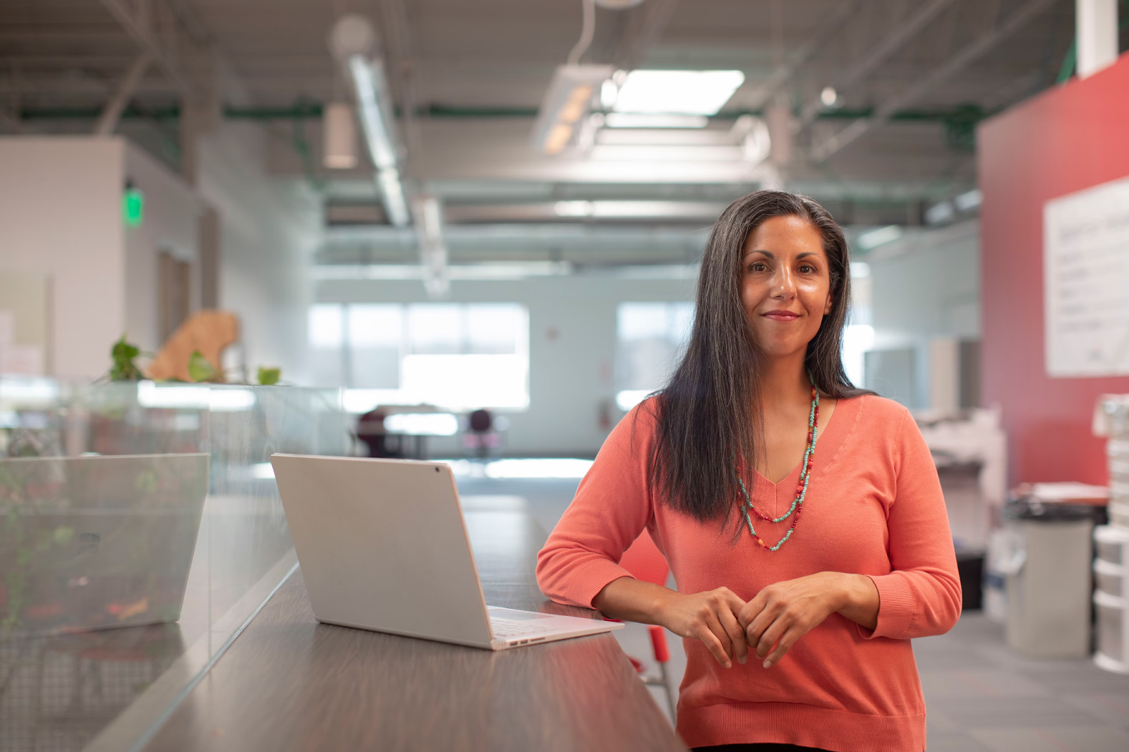 woman leaning on desk with laptop on and smiling