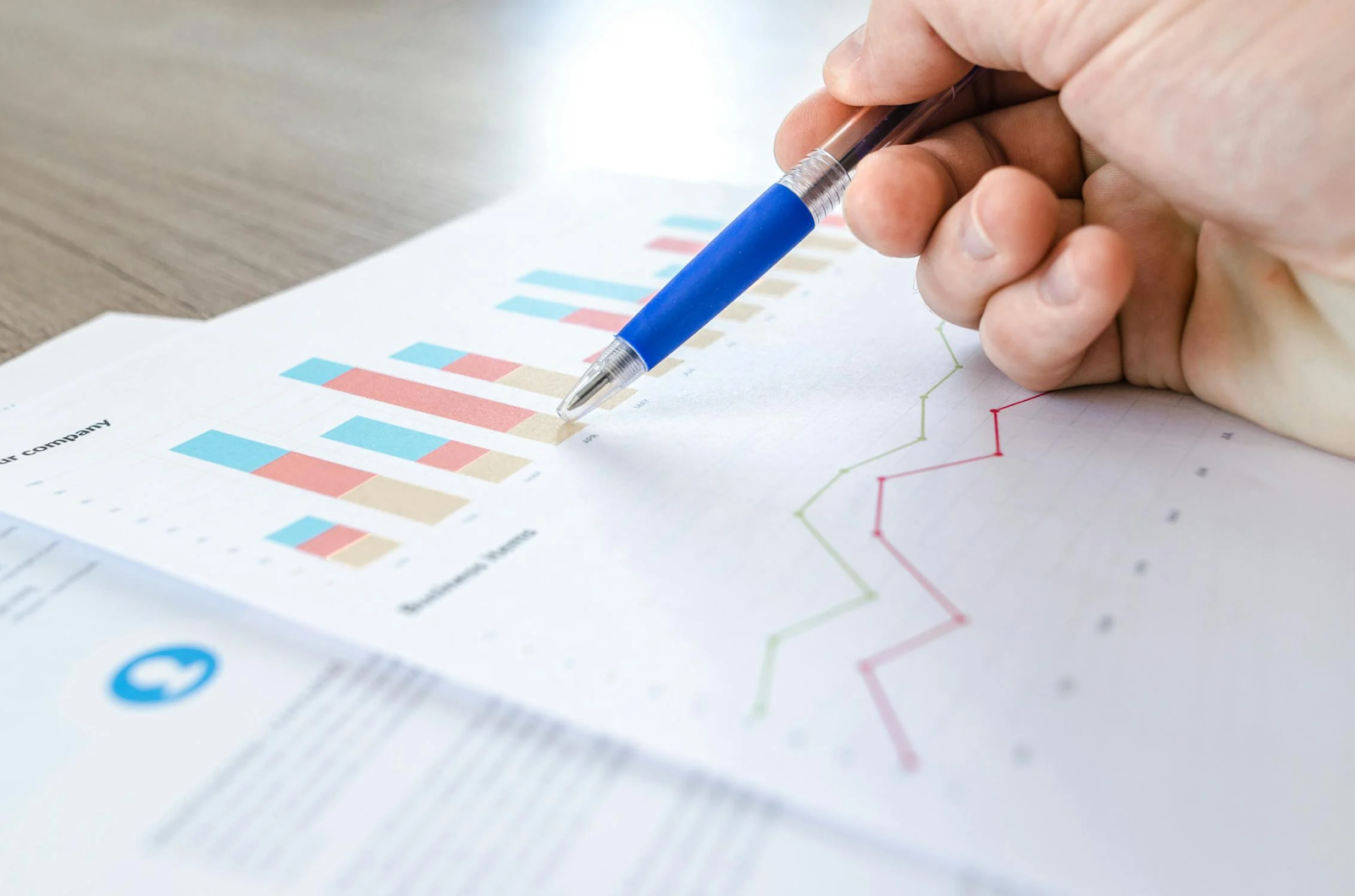 person's hand holding pen at graphs on paper