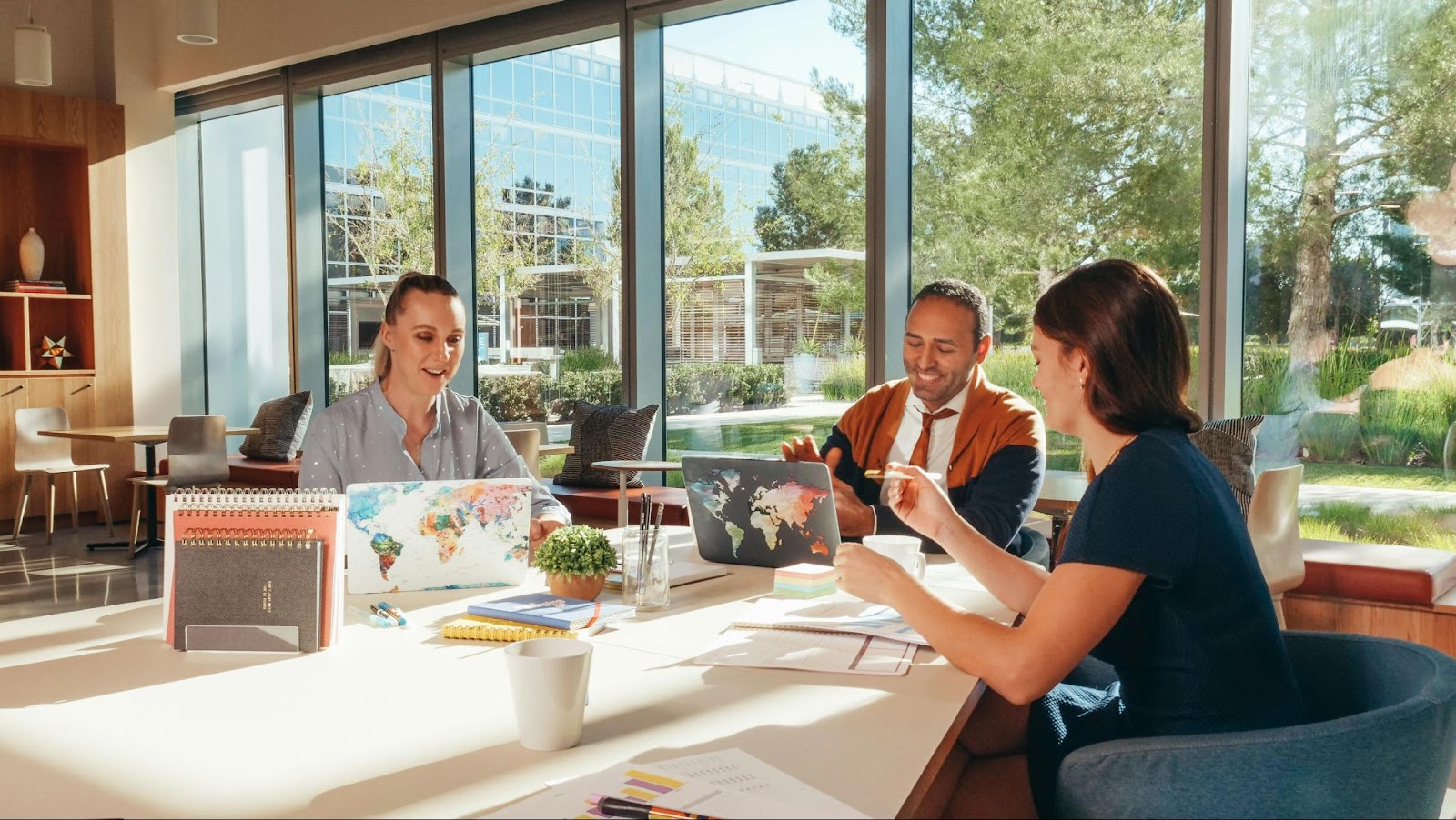 3 people sat at desk working, with big windows behind them