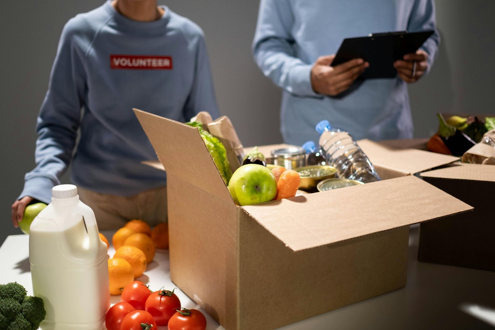 boxes of food on table in front of two people wearing blue sweatshirts with 'volunteer' on them