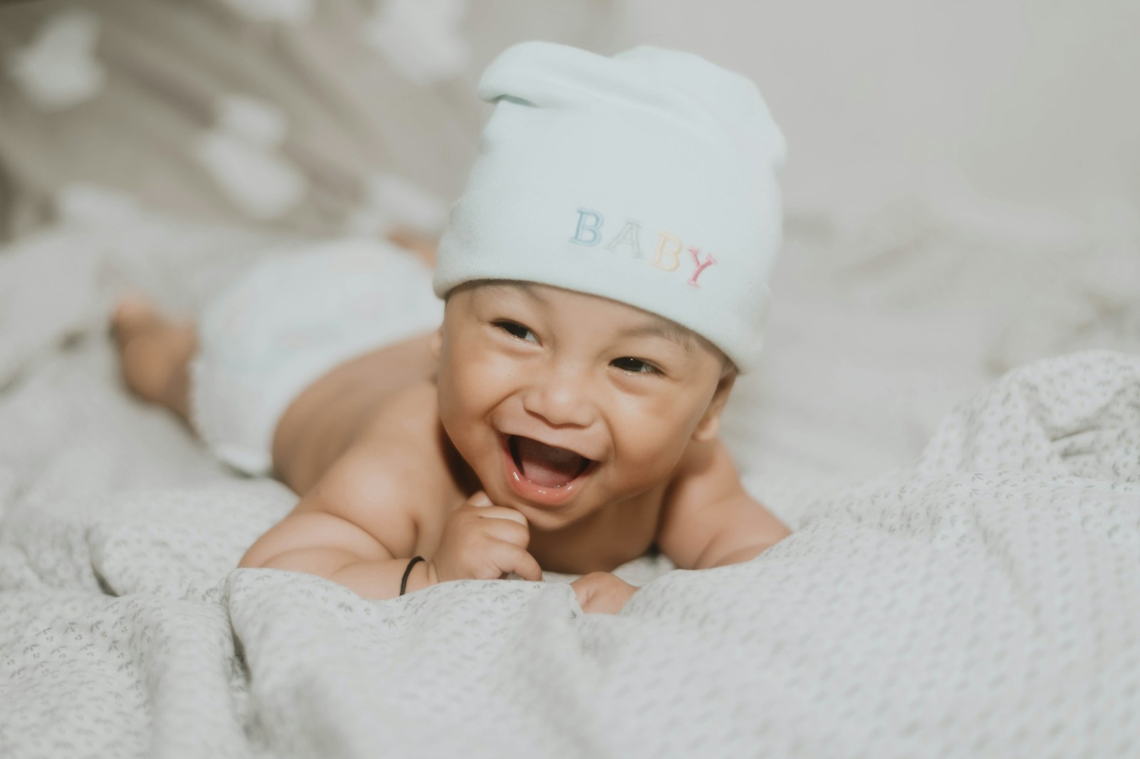 a baby wearing a white hat lying on their front and laughing