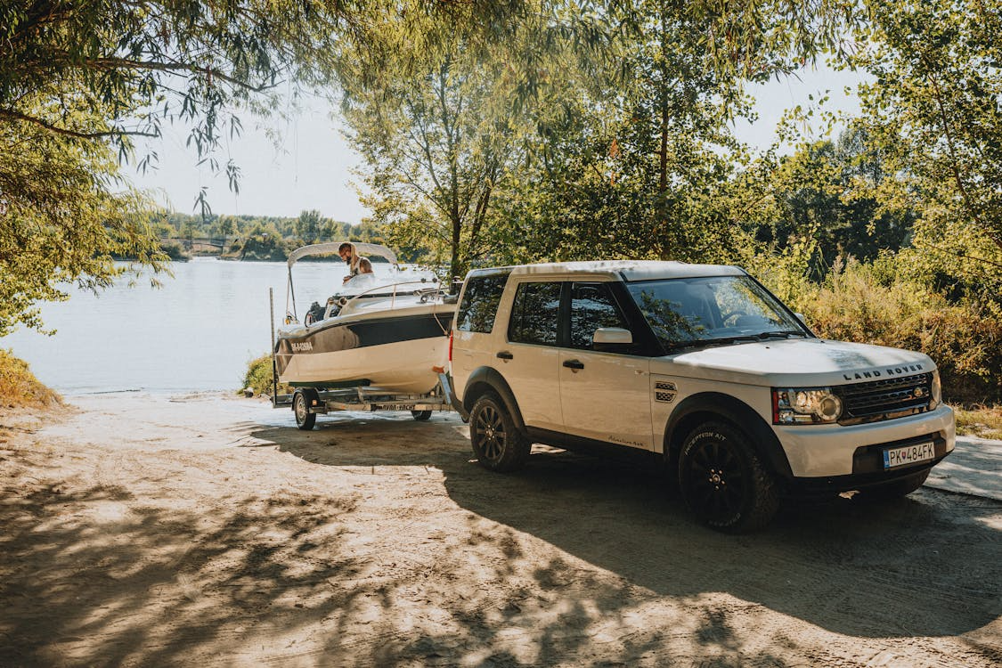 land rover with a boat attahced to the back next to a lake