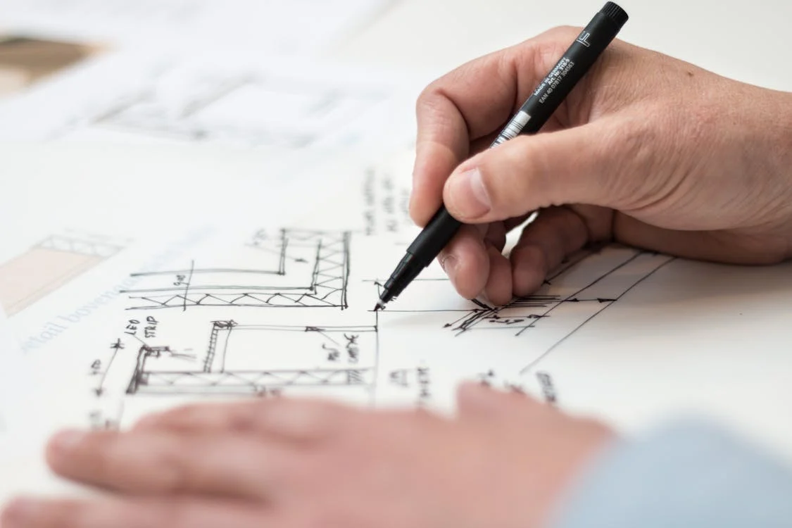 person's hands holdign a pen and writing on renovation plans on paper