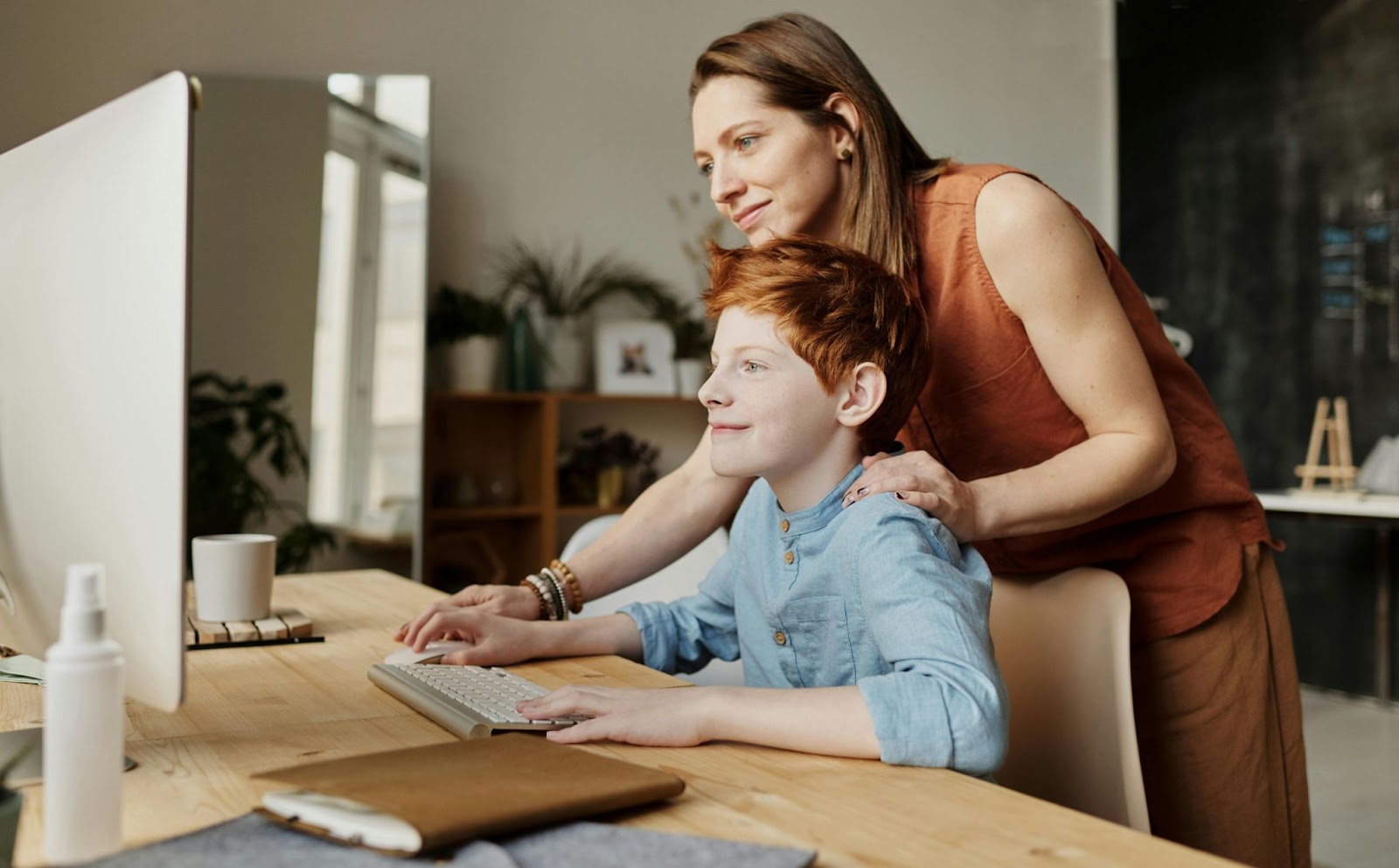 boy with red hair on computer with mum behind him and both smiling