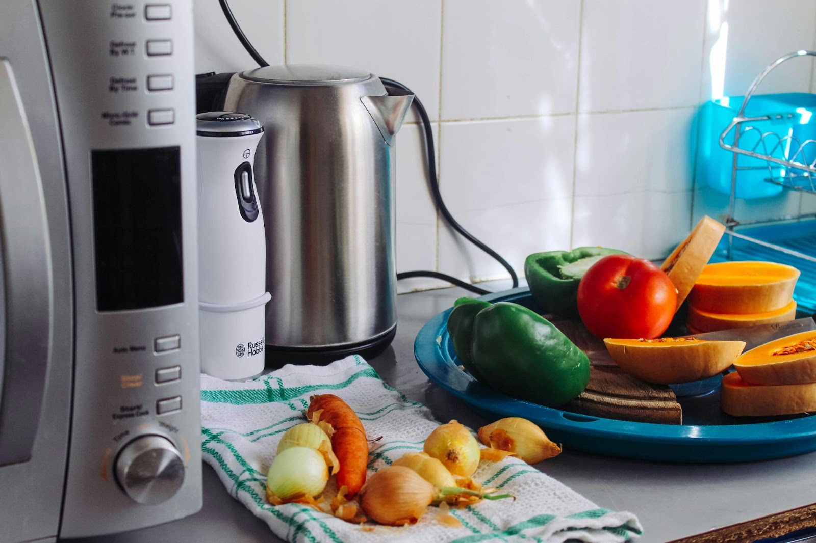 vegetables on kitchen worktop on plate and tea towel, with kitchen appliances next to them