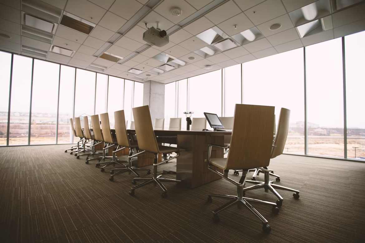 large empty meeting room with long table with chairs lined up around it, and large windows around the sides