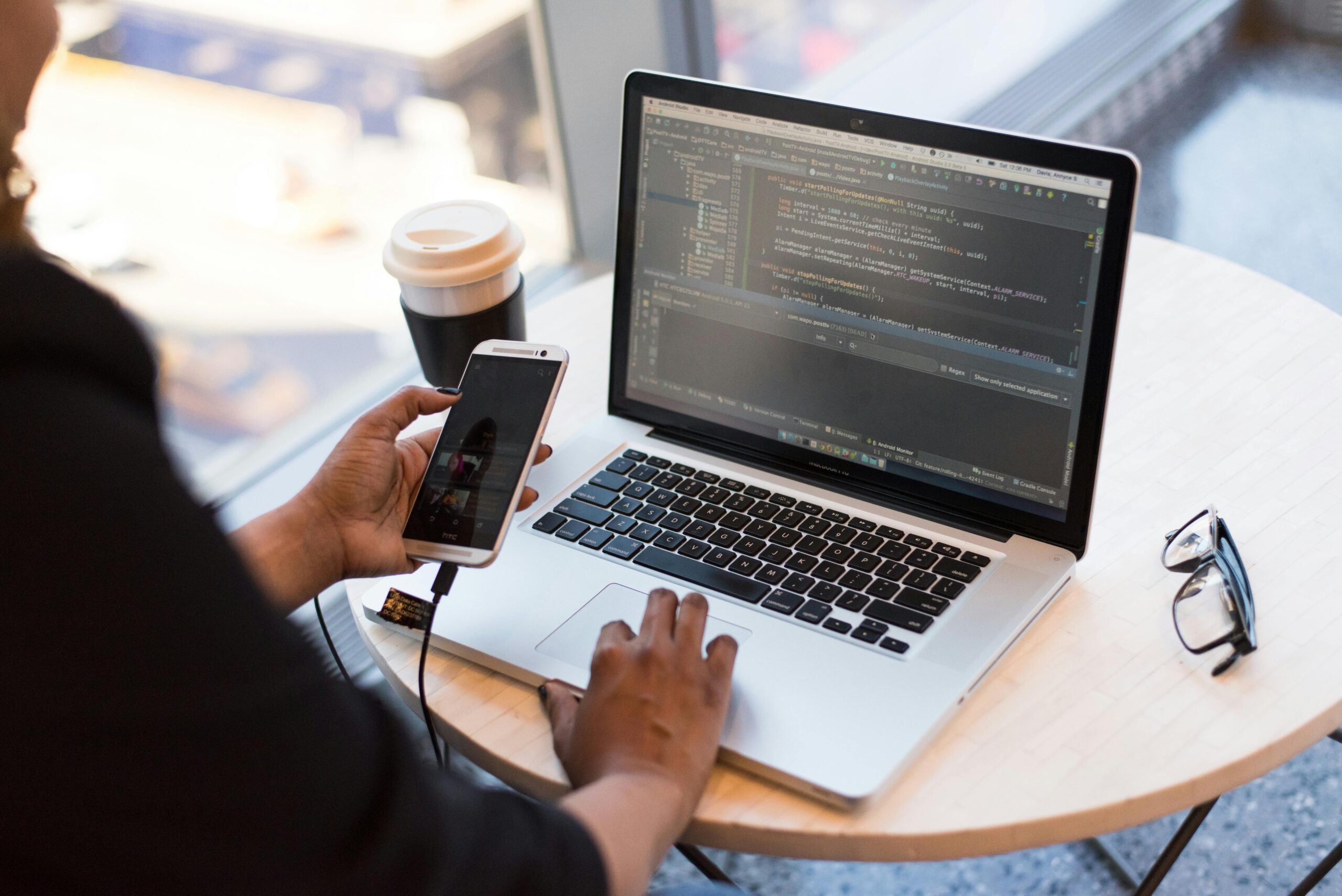 person sitting at laptop in cafe with phone in hand