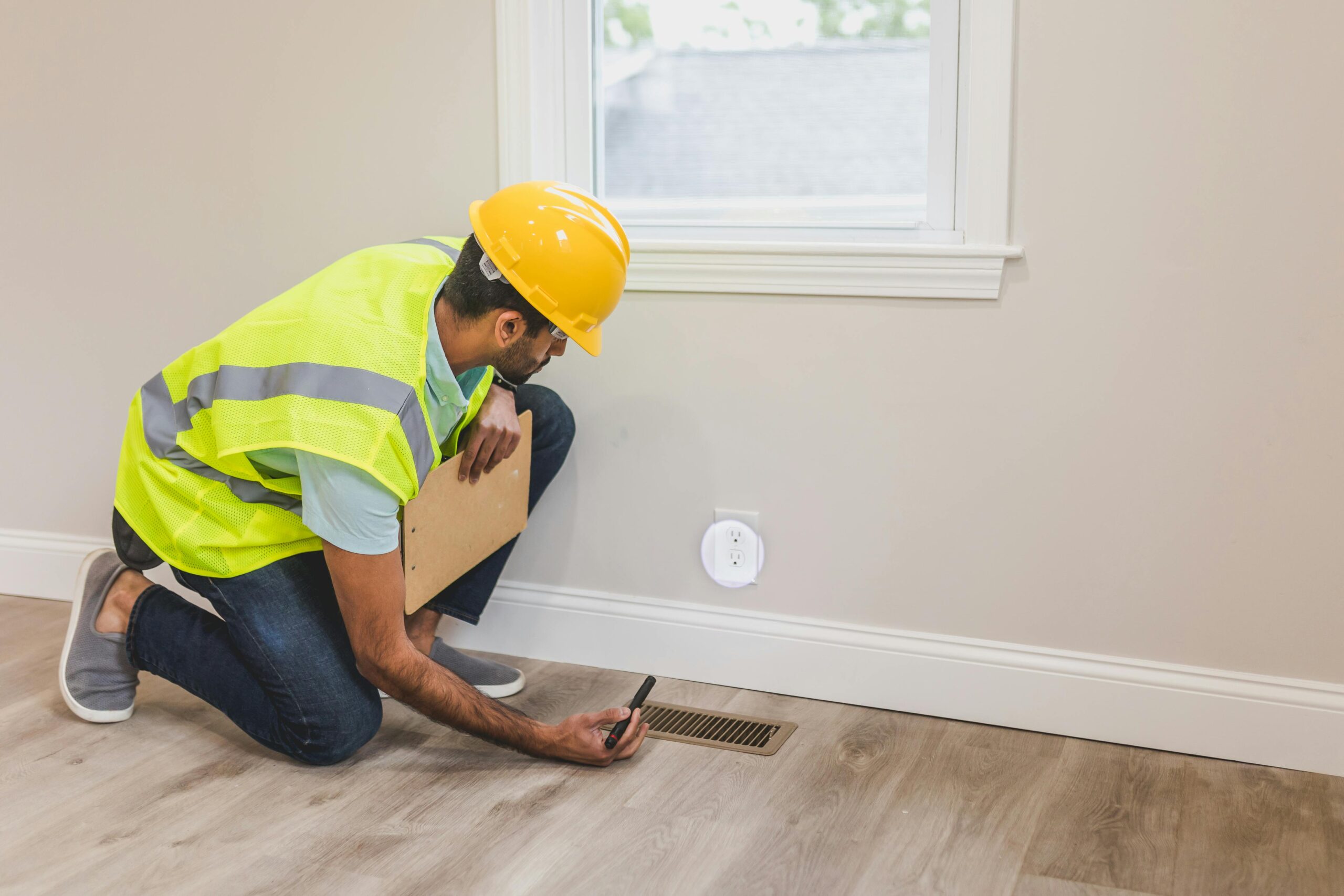 man wearing hi vis vest and yellow helmet bending down against wall in house