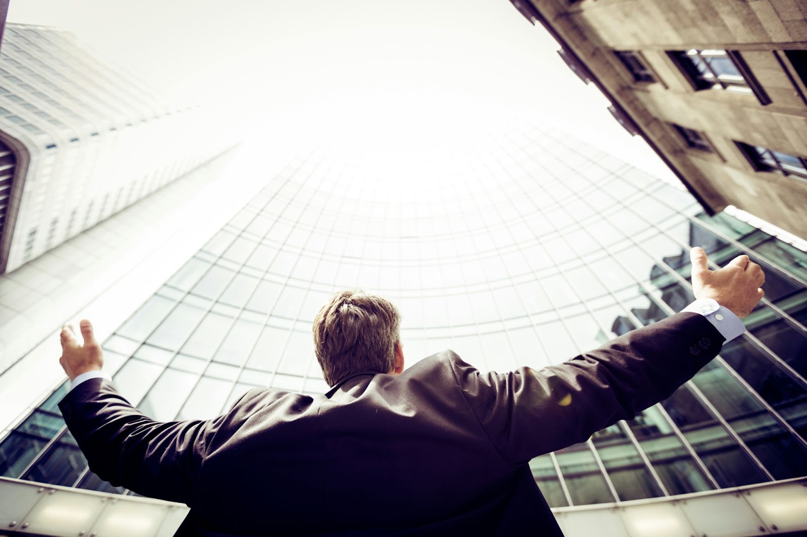 man outside building, reaching arms up towards it