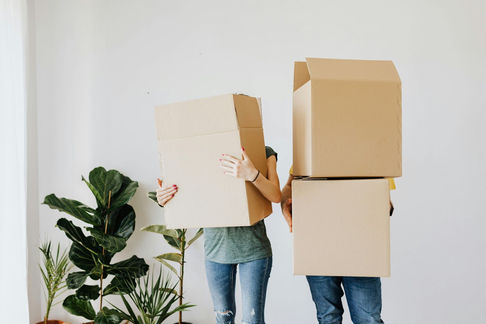 two people standing with empty moving boxes in their arms in front of their faces