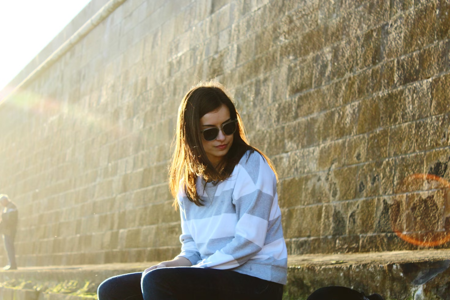 woman wearing sunglasses and stripey jumper sitting on concrete steps next to brick wall