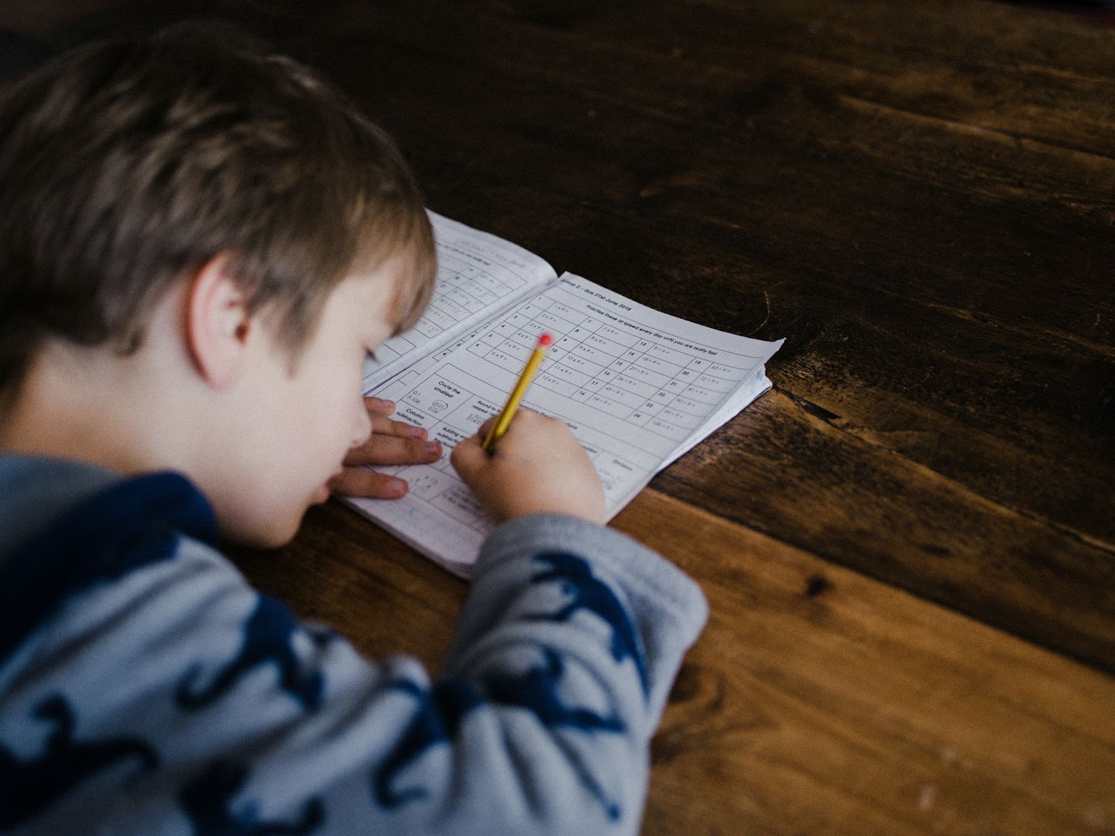 boy writing on workbook on table