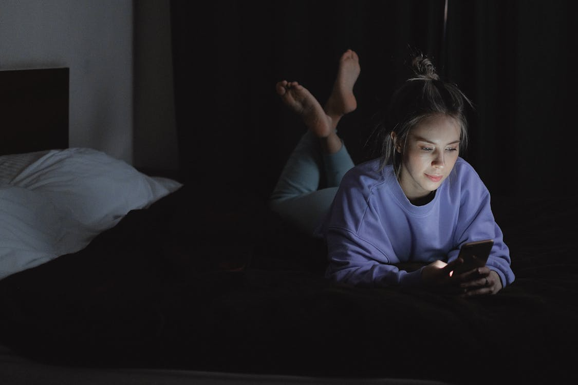 woman lying on her front on bed in darkness on her phone