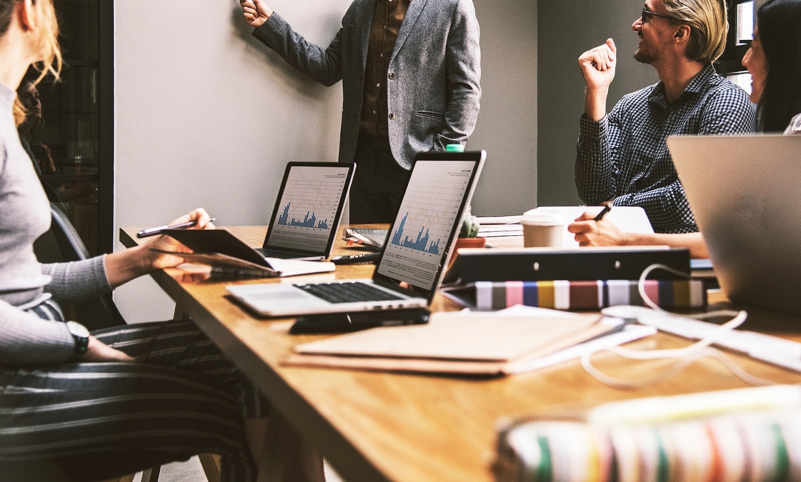 people sitting around a table for a business meeting, with one person stood at the front pointing to a whiteboard
