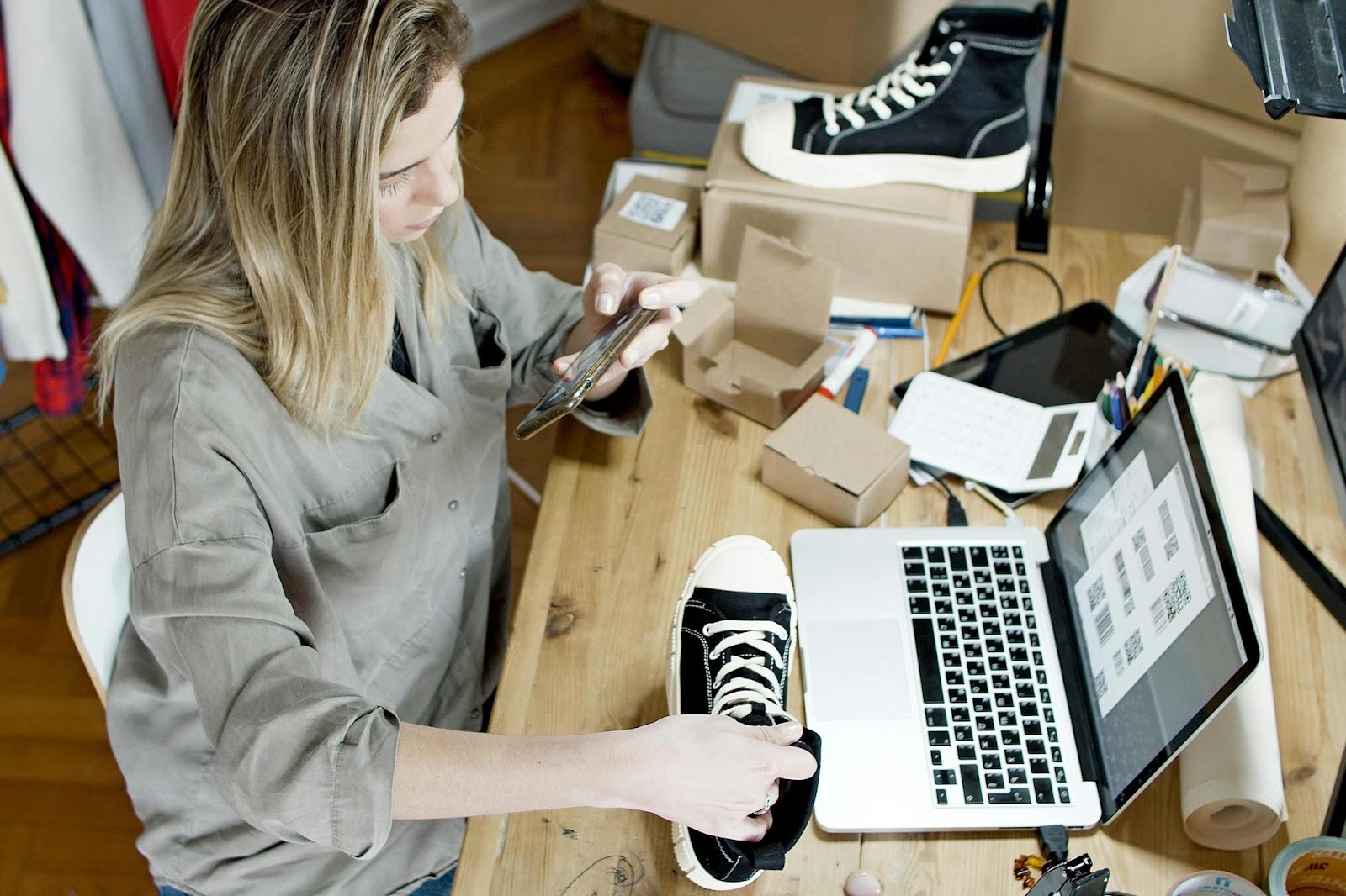 Woman taking photo of shoes next to laptop on desk