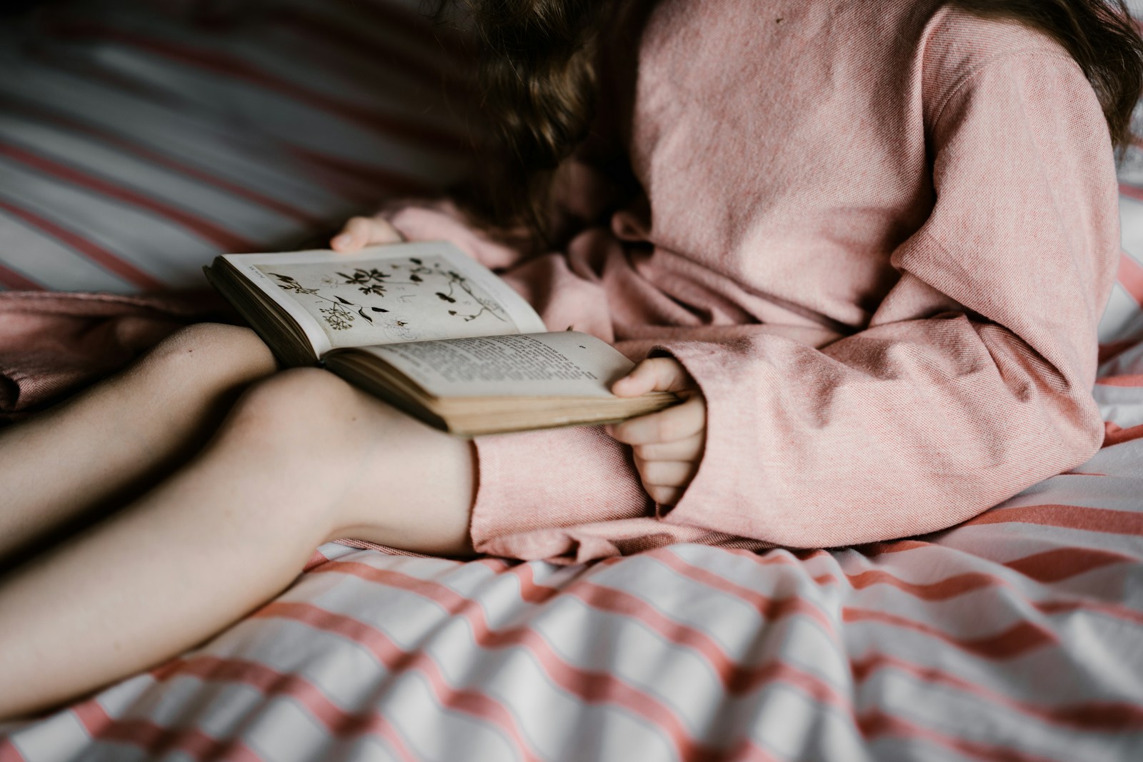 girl reading book on white and red bed cover