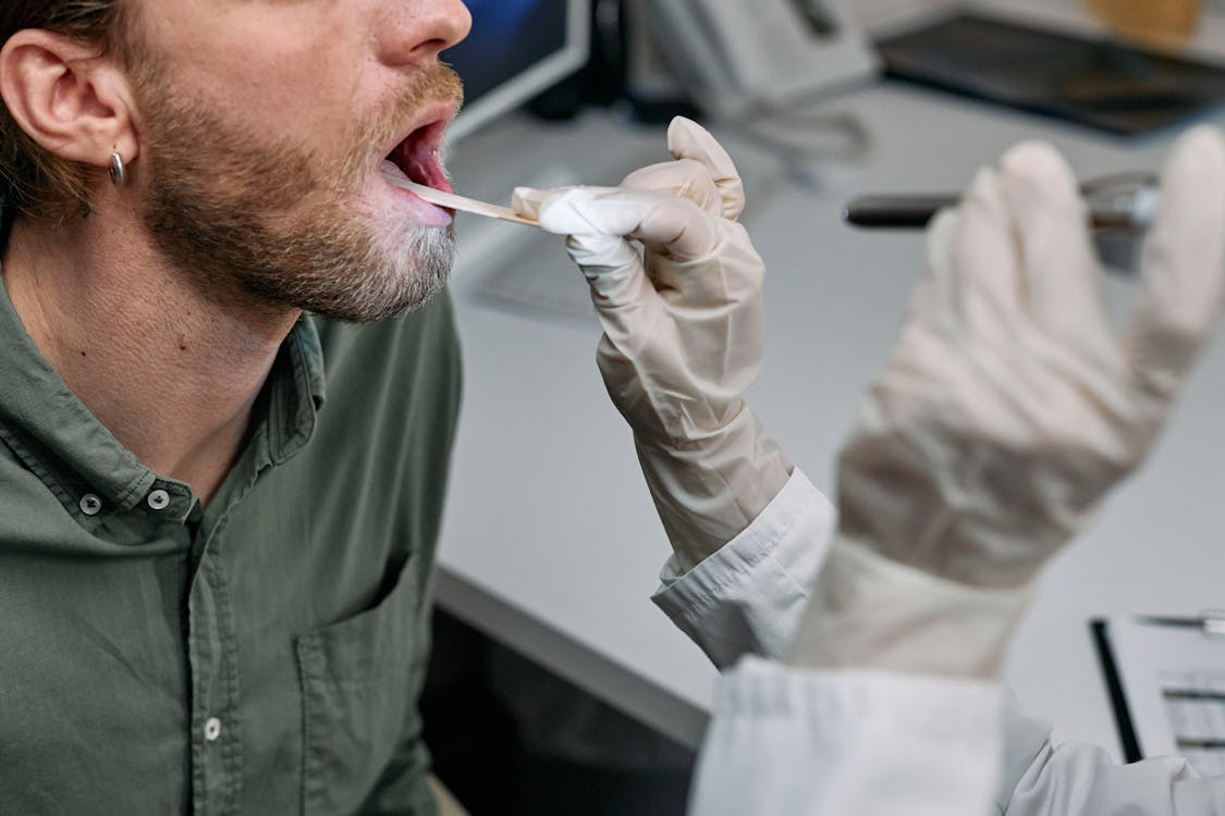 dentist wearing white latex glove looking into mouth of male patient