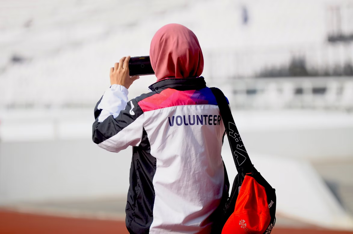 woman wearing headscarf and a volunteer jacket holding phone up to take a photo