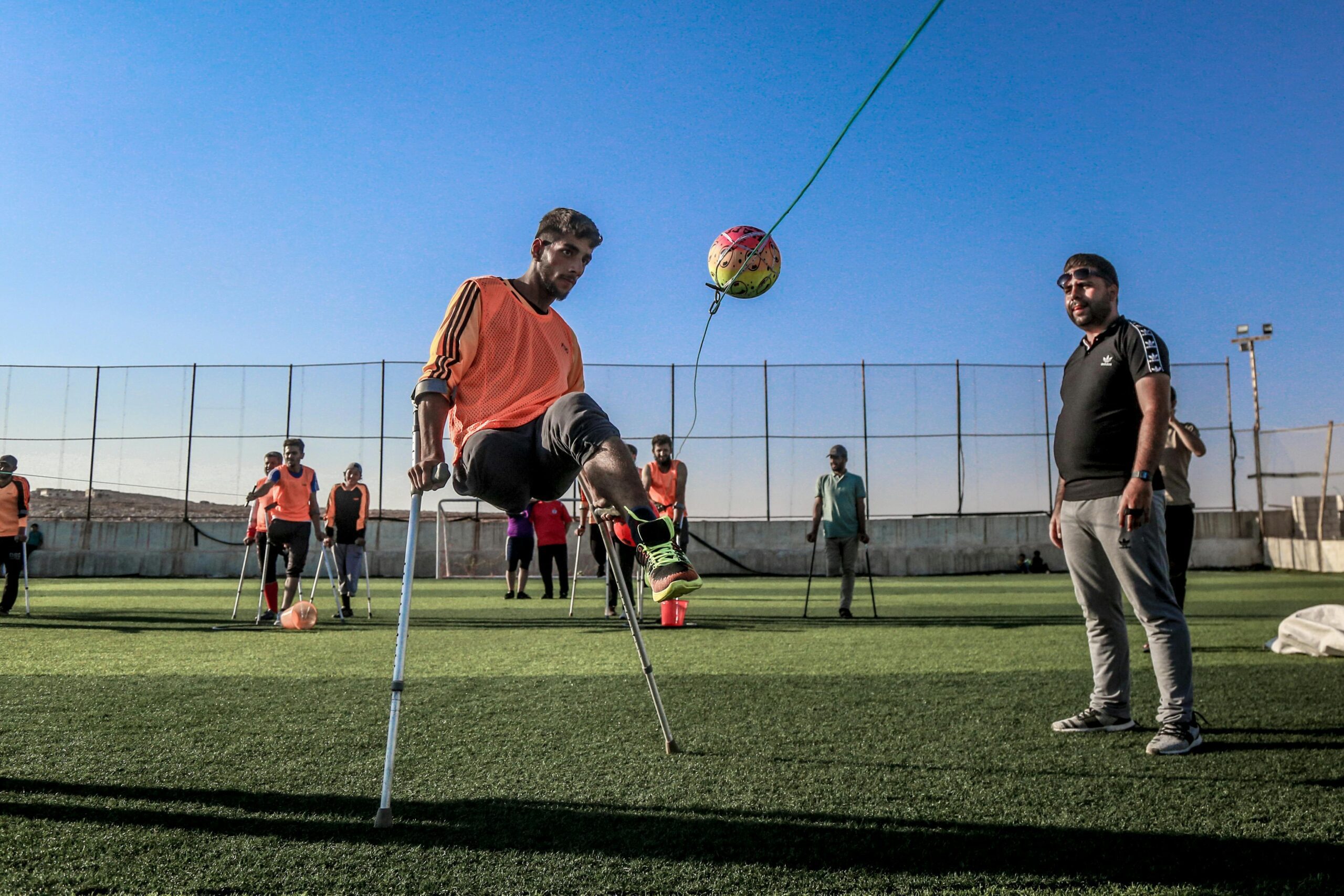 disabled man with walking sticks kicking a football on pitch