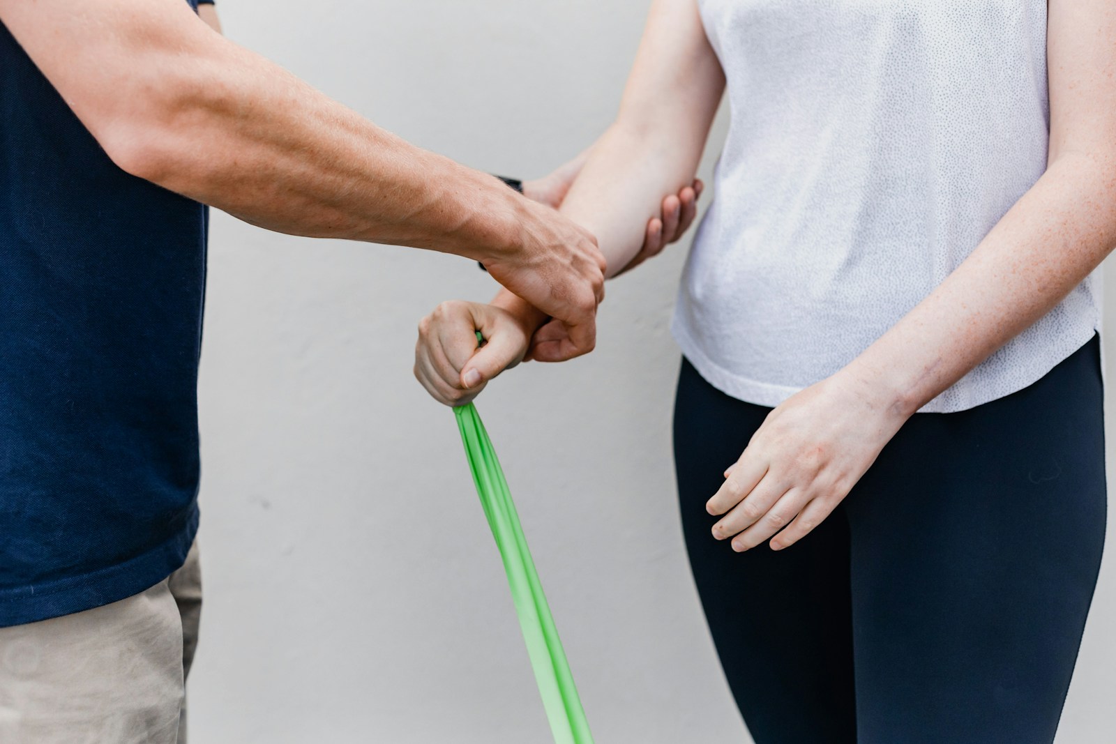 a man and a woman with the woman holding a green band for stretching and the man holding onto her arm