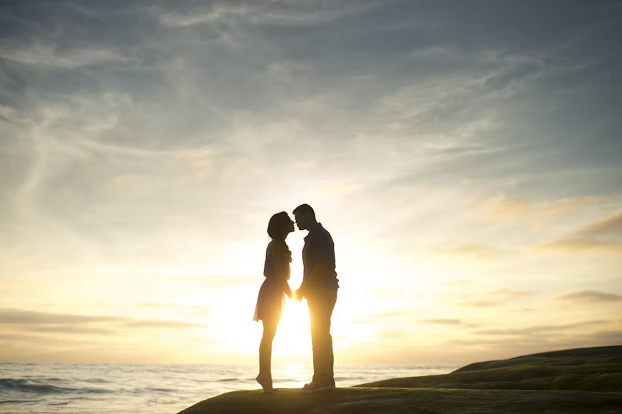 couple standing on hill in sunlight, facing each other, holding hands and kissing