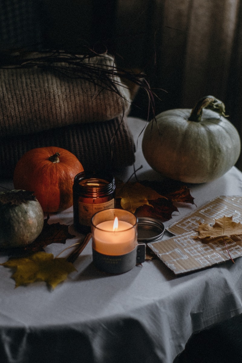 a table topped with a litcandle next to a pile of pumpkins