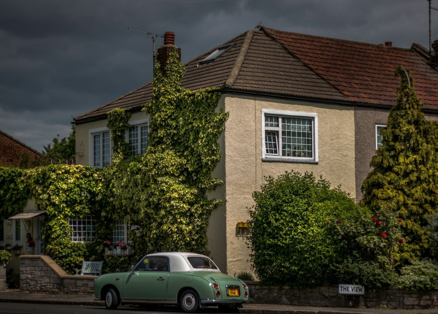 green and white coupe parked outside of large house with green trees outside