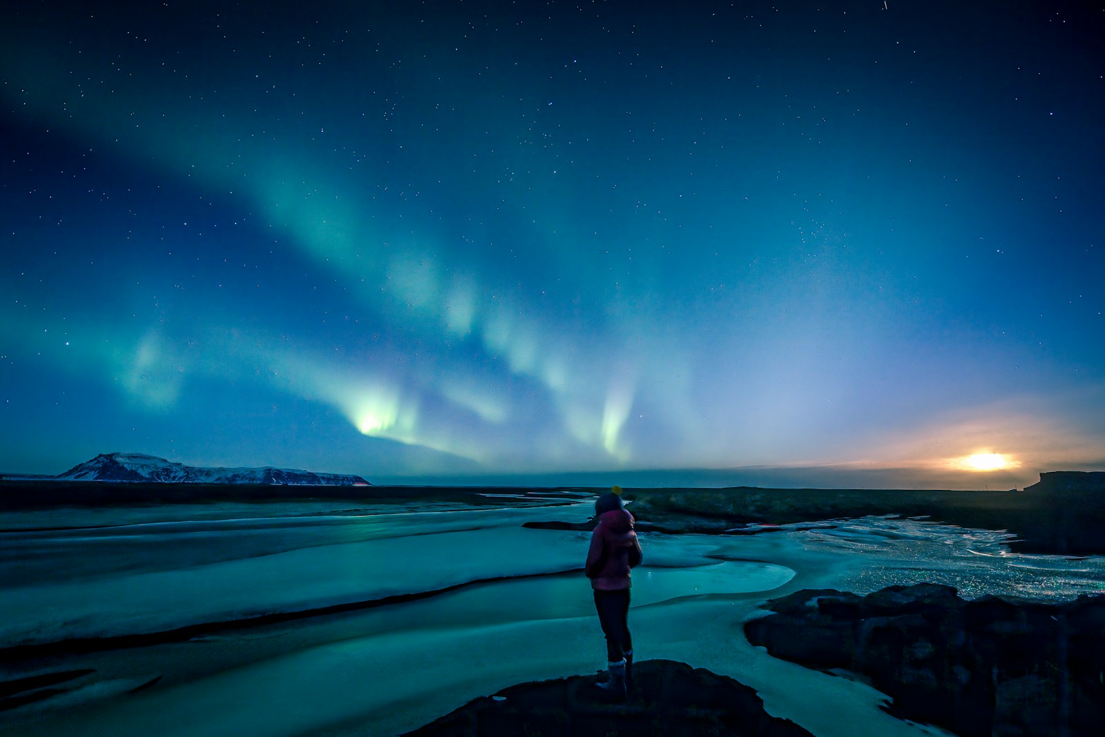 man standing on rock formation under northern lights during night time