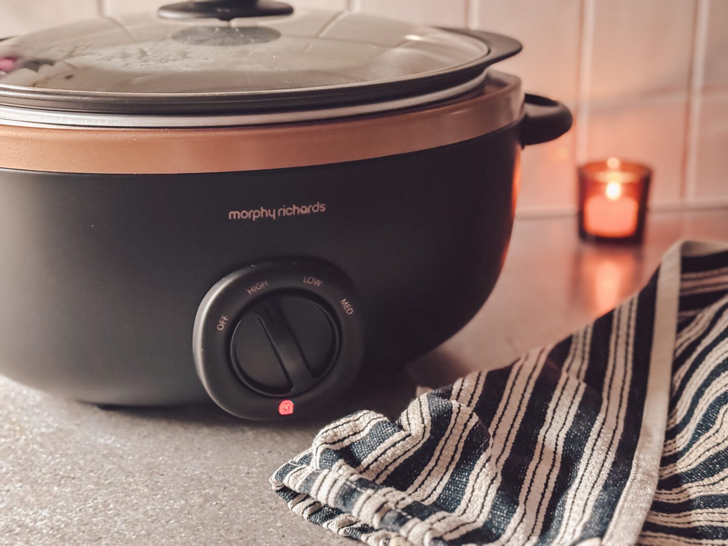 slow cooker on kitchen side next to tea towel and wooden spoon with candlle in background