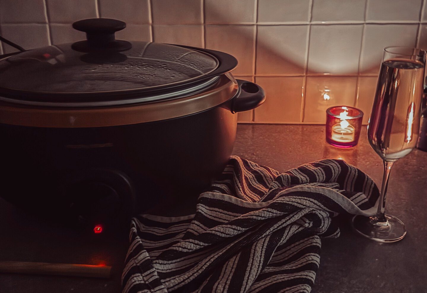 slow cooker on kitchen side next to tea towel and wooden spoon with candlle in background
