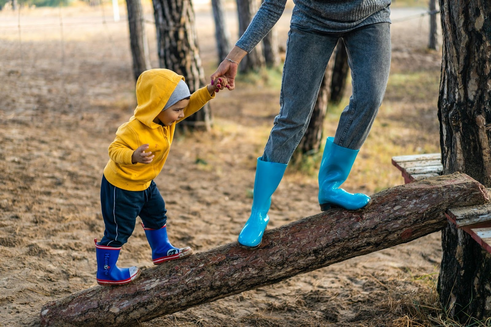 mother and son wearing wellies, climbing up a log in the woods
