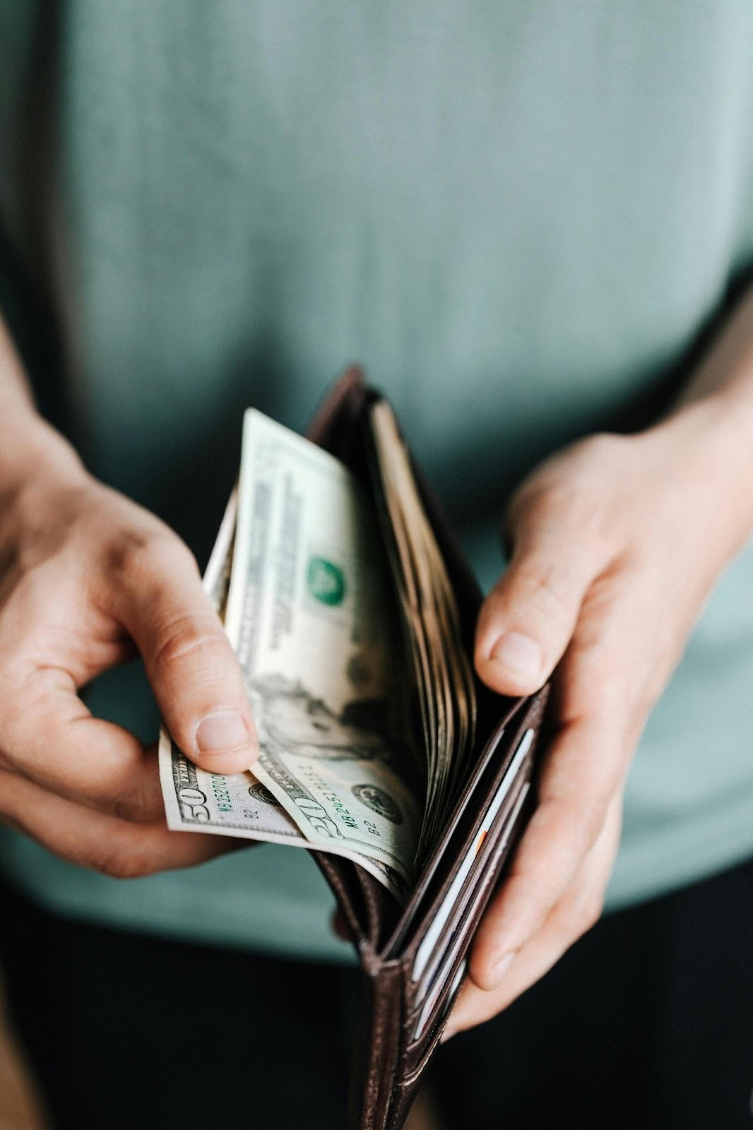 person waring green t-shirt holiding wallet full of cash in hands