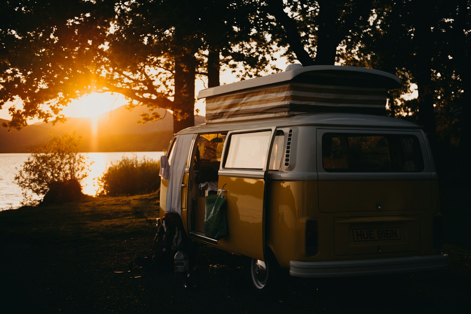 brown and white campervan under trees during sunset