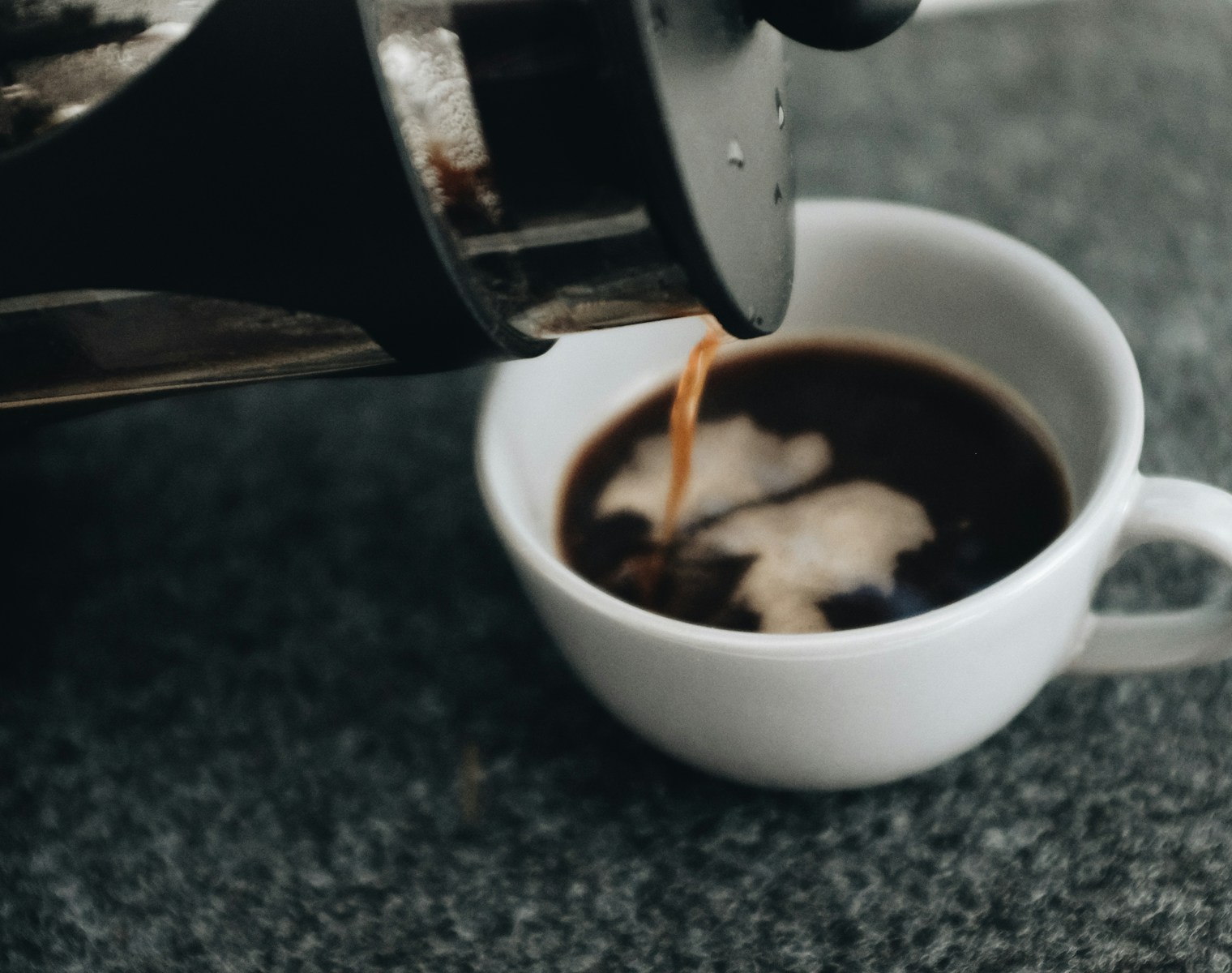 a cup of coffee being poured into a mug from a cafetiere