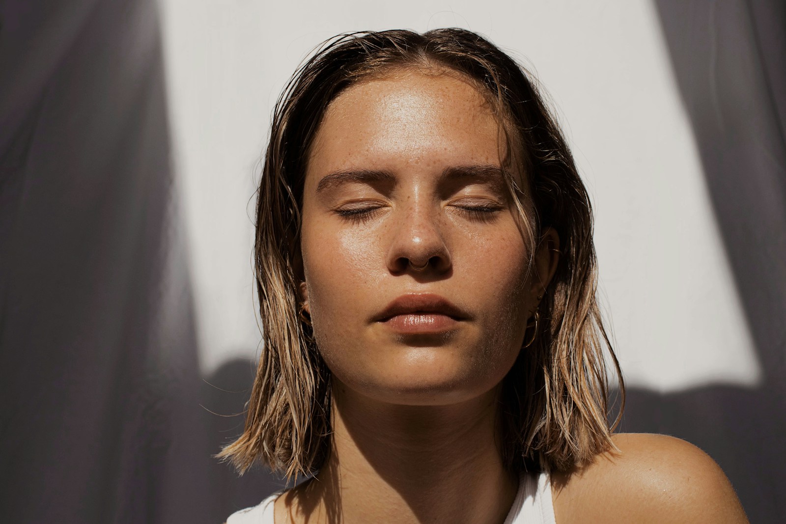 woman in white tank top with eyes closed and facing the sun